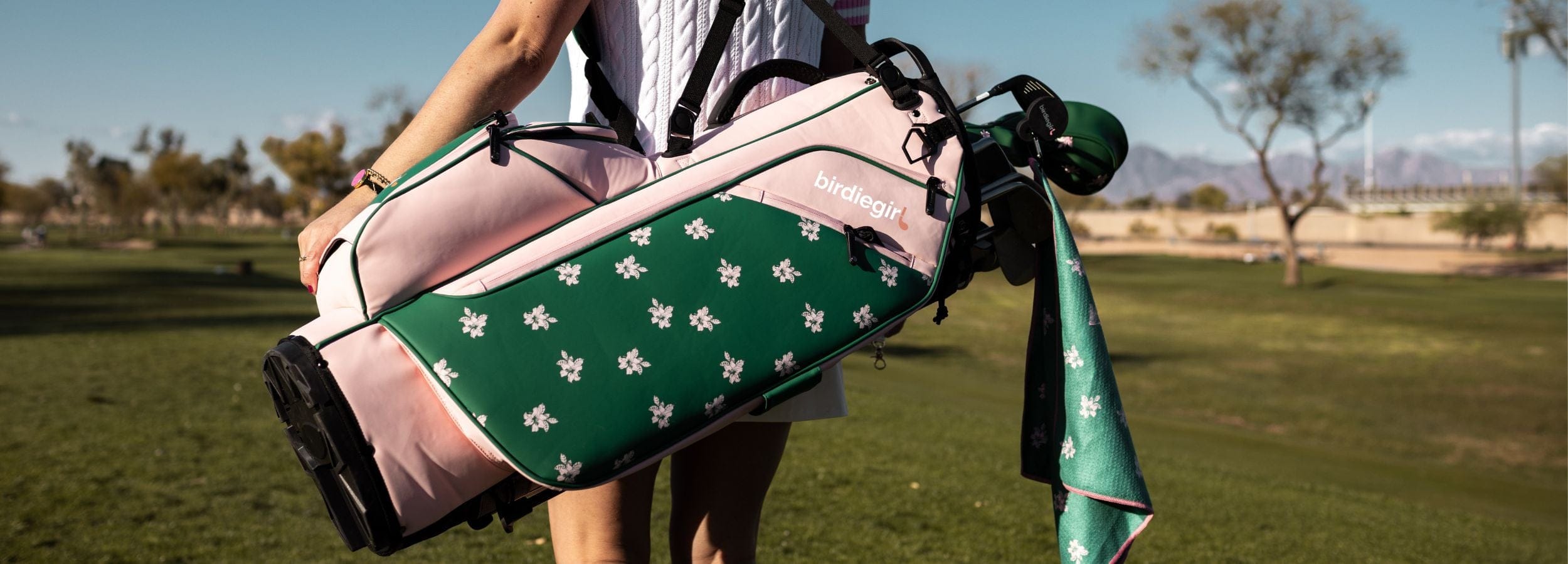 Woman holding a golf bag with a green and pink design on a golf course
